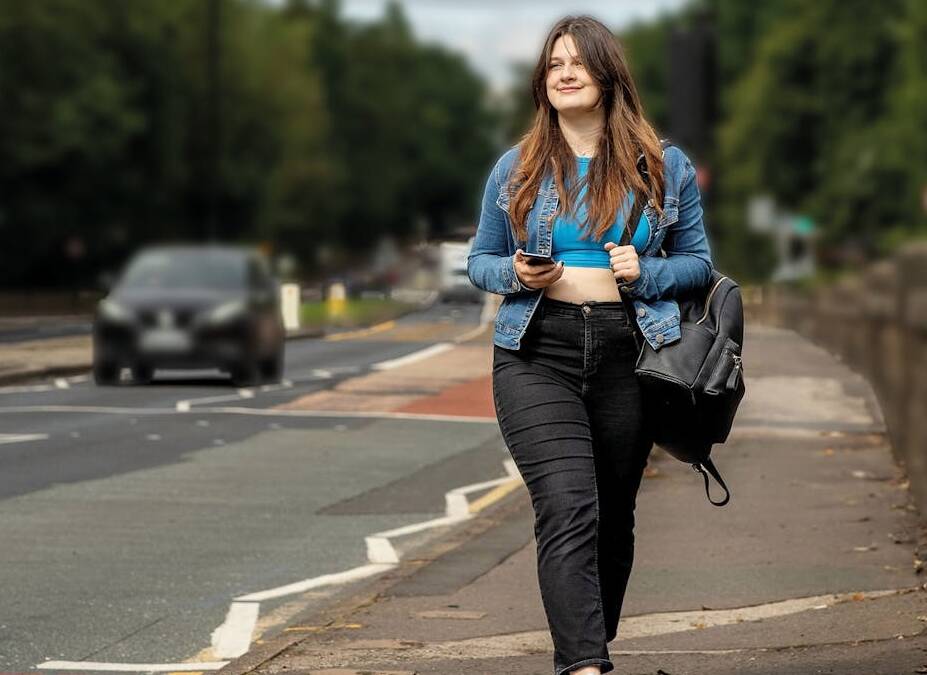 Woman walking on pavement beside road