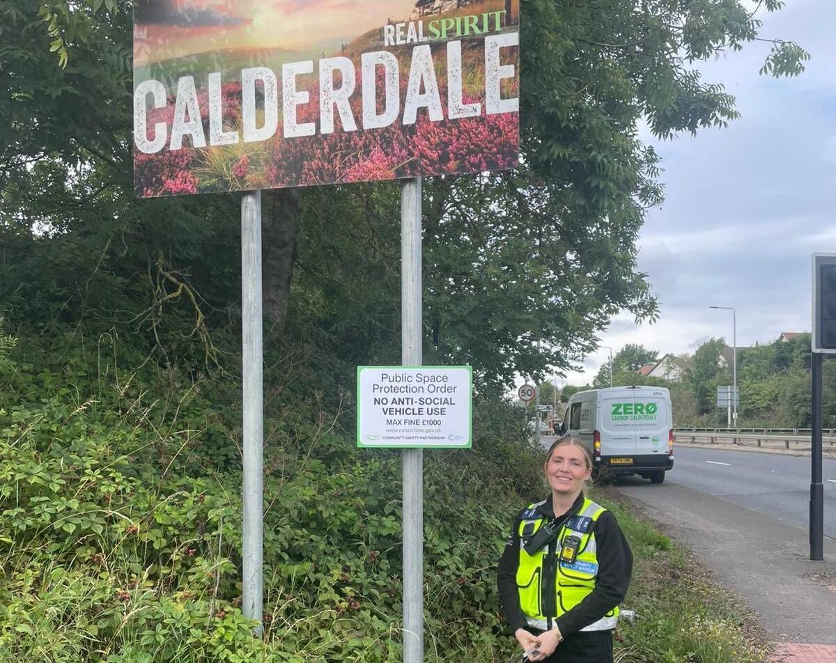 Community Safety Warden at the side of the road with a sign saying no anti-social vehicle use allowed