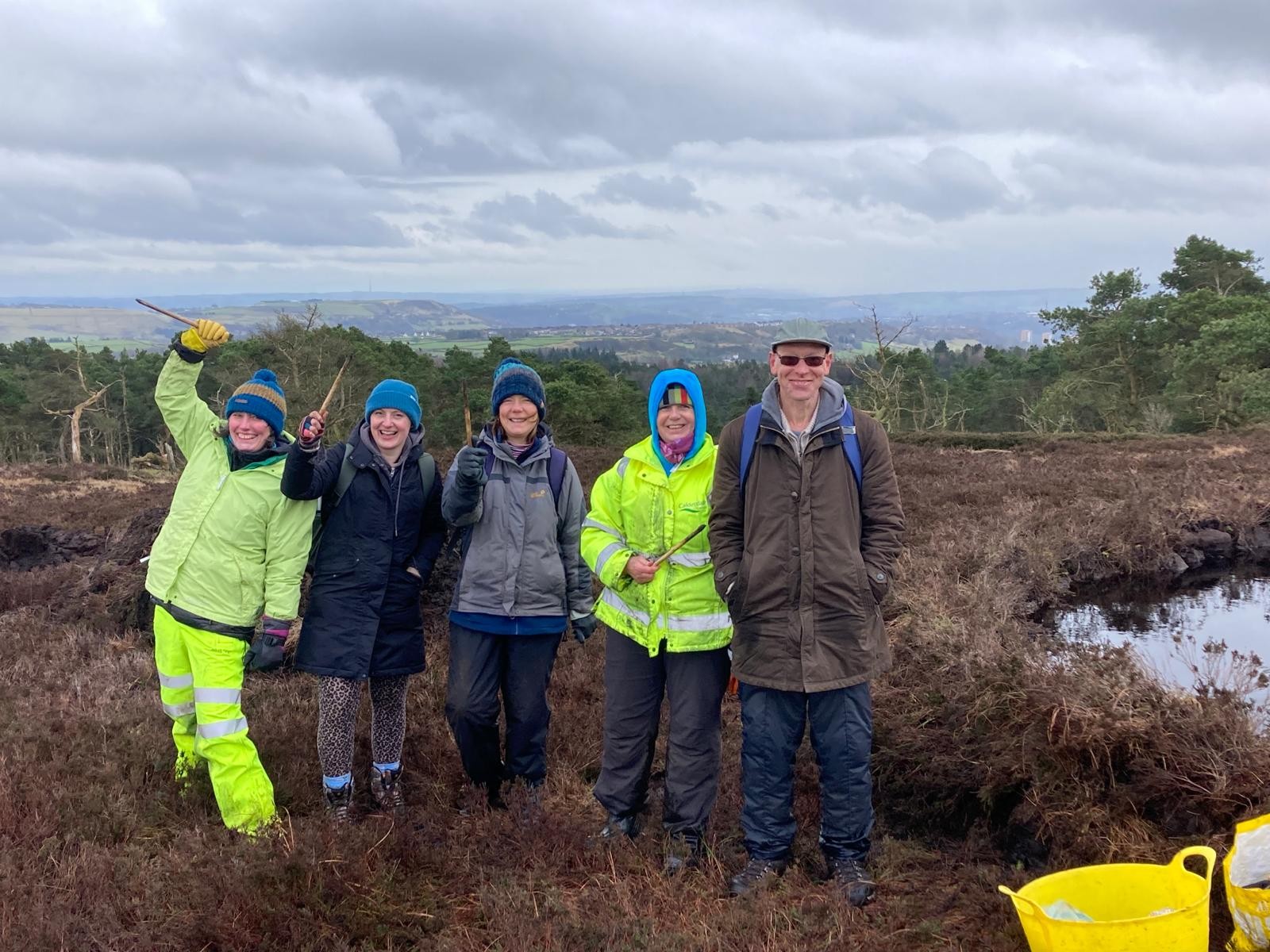 Group of people on Calderdale moorland holding planting equipment and smiling